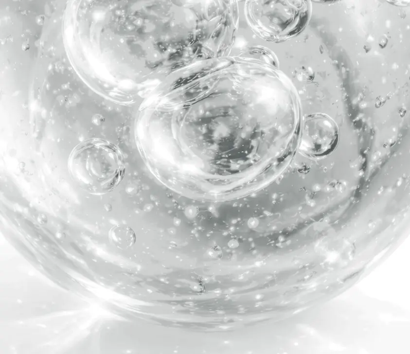 Close-up image of clear bubbles suspended in a transparent liquid, surrounded by tiny sparkling particles, creating a bright and glistening abstract effect.
