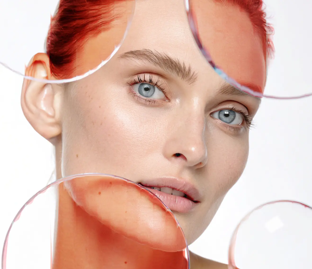 A woman with red hair and blue eyes gazes at the camera. Her skin is glowing, and round, transparent circles with a red tint overlay the image, creating an abstract and artistic effect.