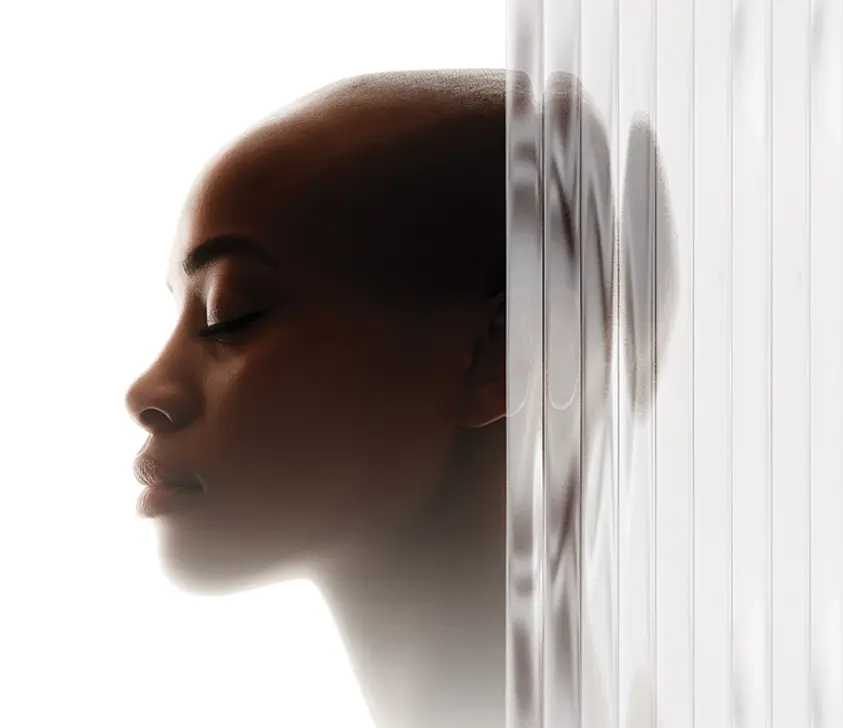 A person with closed eyes and serene expression is shown in profile, with their head partly obscured by a frosted, ribbed glass panel that distorts their reflection on the right side of the image.