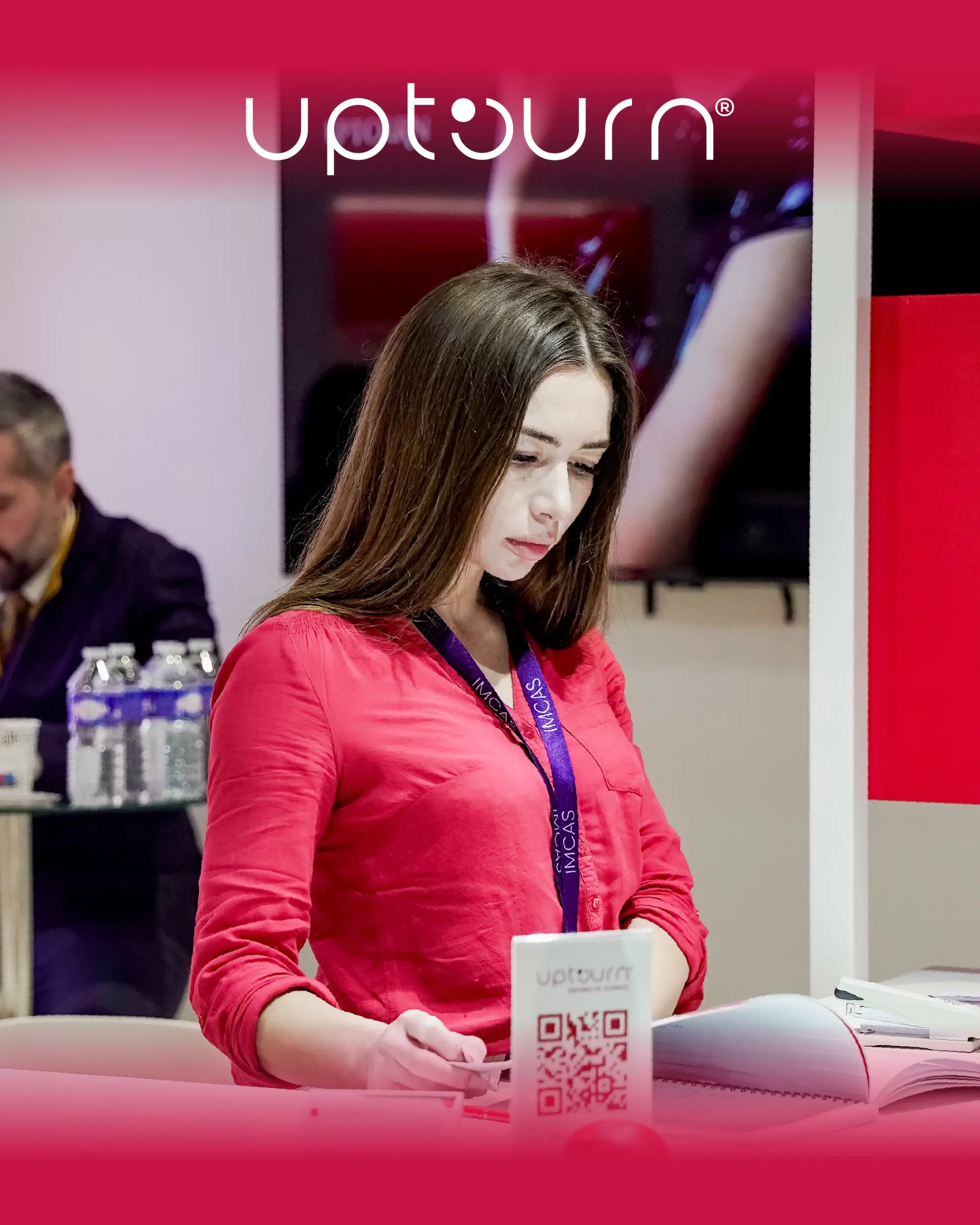 A woman in a red shirt reads a book at a table, with a white upturn-branded cup in front of her. The word "upturn" appears at the top of the image, and two people sit in the blurred background.