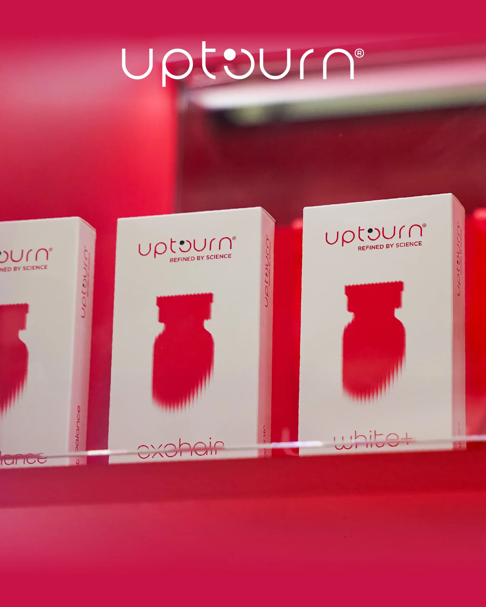 Three white boxes of Upturn supplements with red accents and bottle silhouettes are displayed on a glass shelf against a bright red background. The Upturn logo appears at the top of the image.